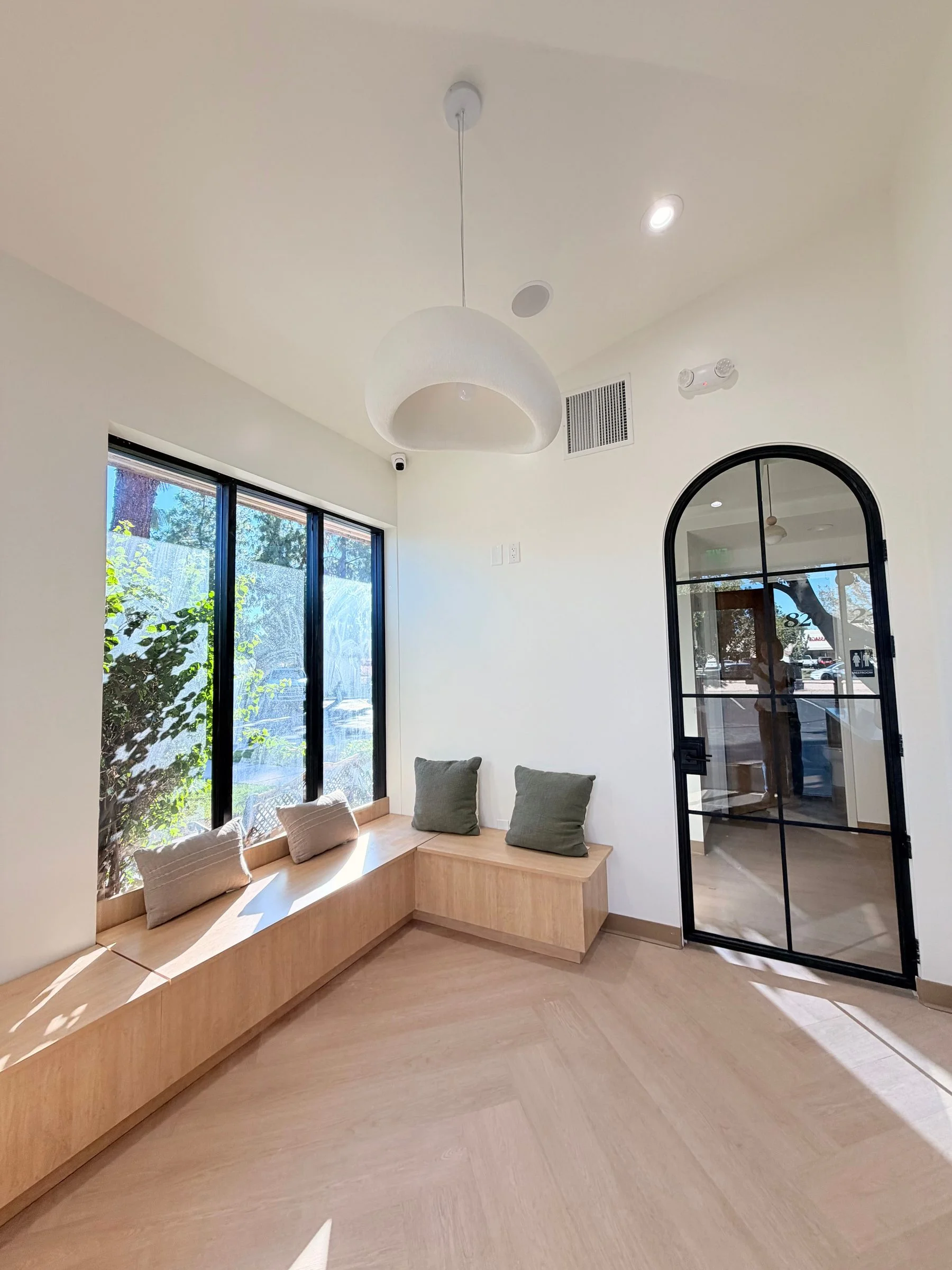 A light wood window seat with pillows under black-framed windows in the renovated Dobson Ranch office.